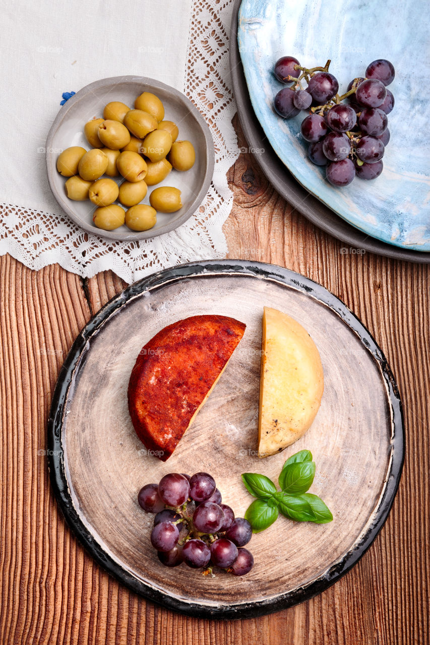 Cheese black grapes and olives decorated with mint on handmade pottery plates on old wooden table from above