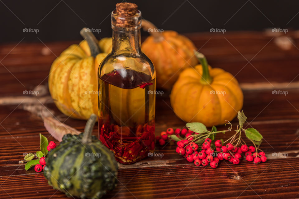 bottle of olive oil with chilli peppers on a rustic table, next to pumpkins, leaves and rowan