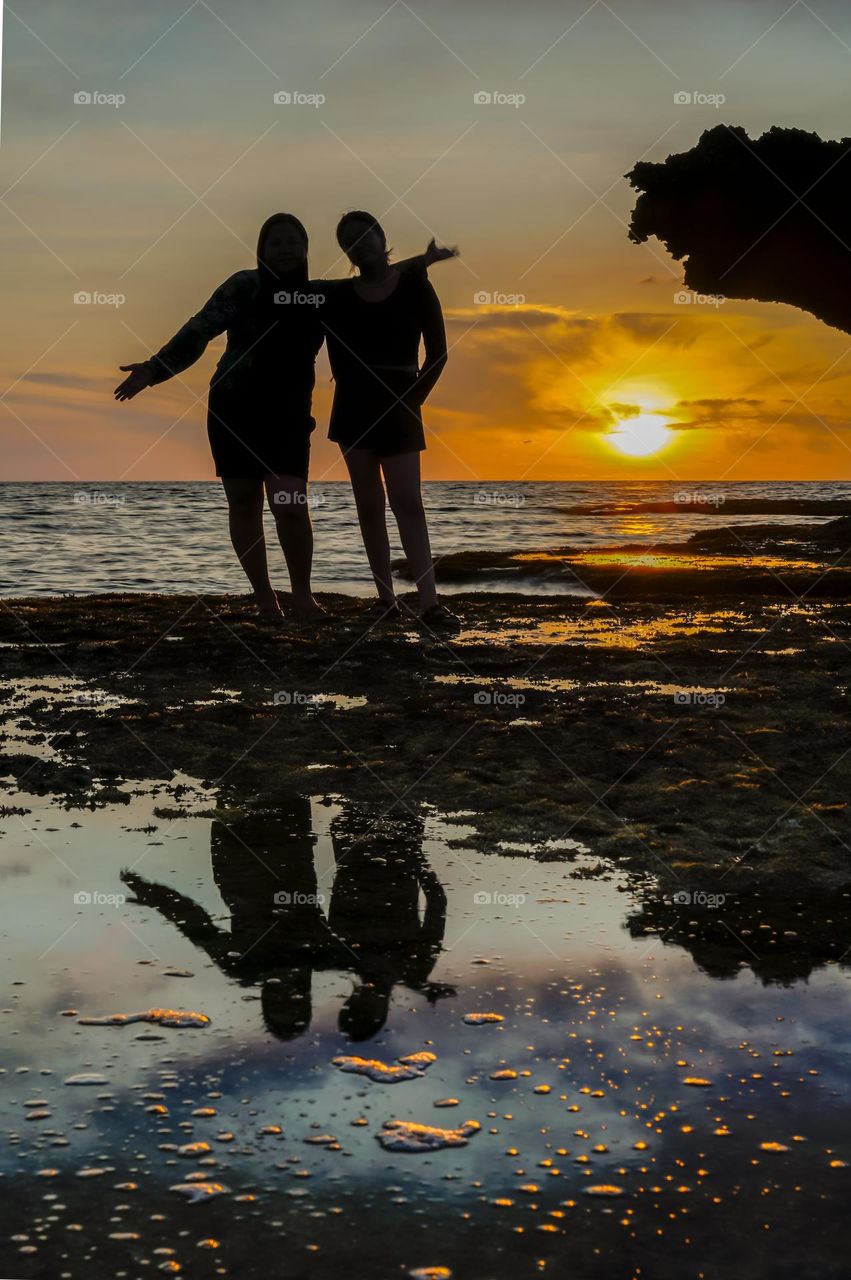 Silhouette and water reflections of a mother and daughter while strolling along the beach during sunset.