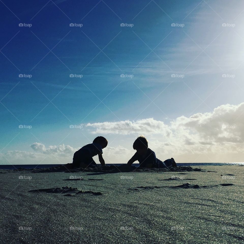Silhouettes of two boys playing in the sand 