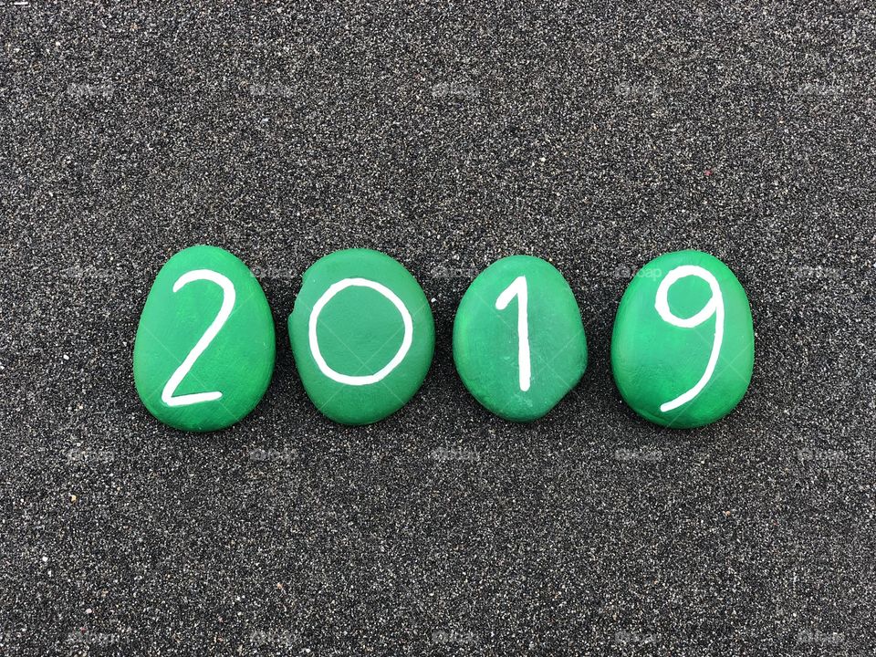 2019 year composed with green painted sea stones over black volcanic sand