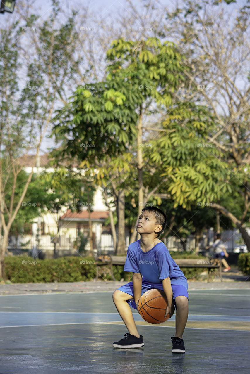 Asian boy holding a basketball ball Background blurry trees.
