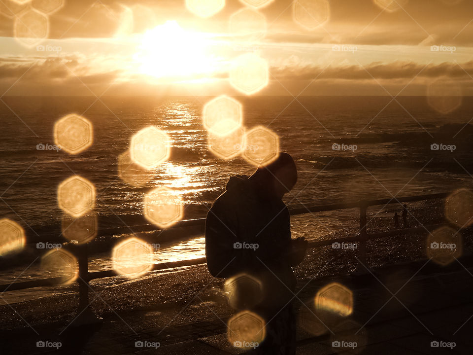 Sunset over the sea with sunrays and lens halo effect and with a person in foreground.