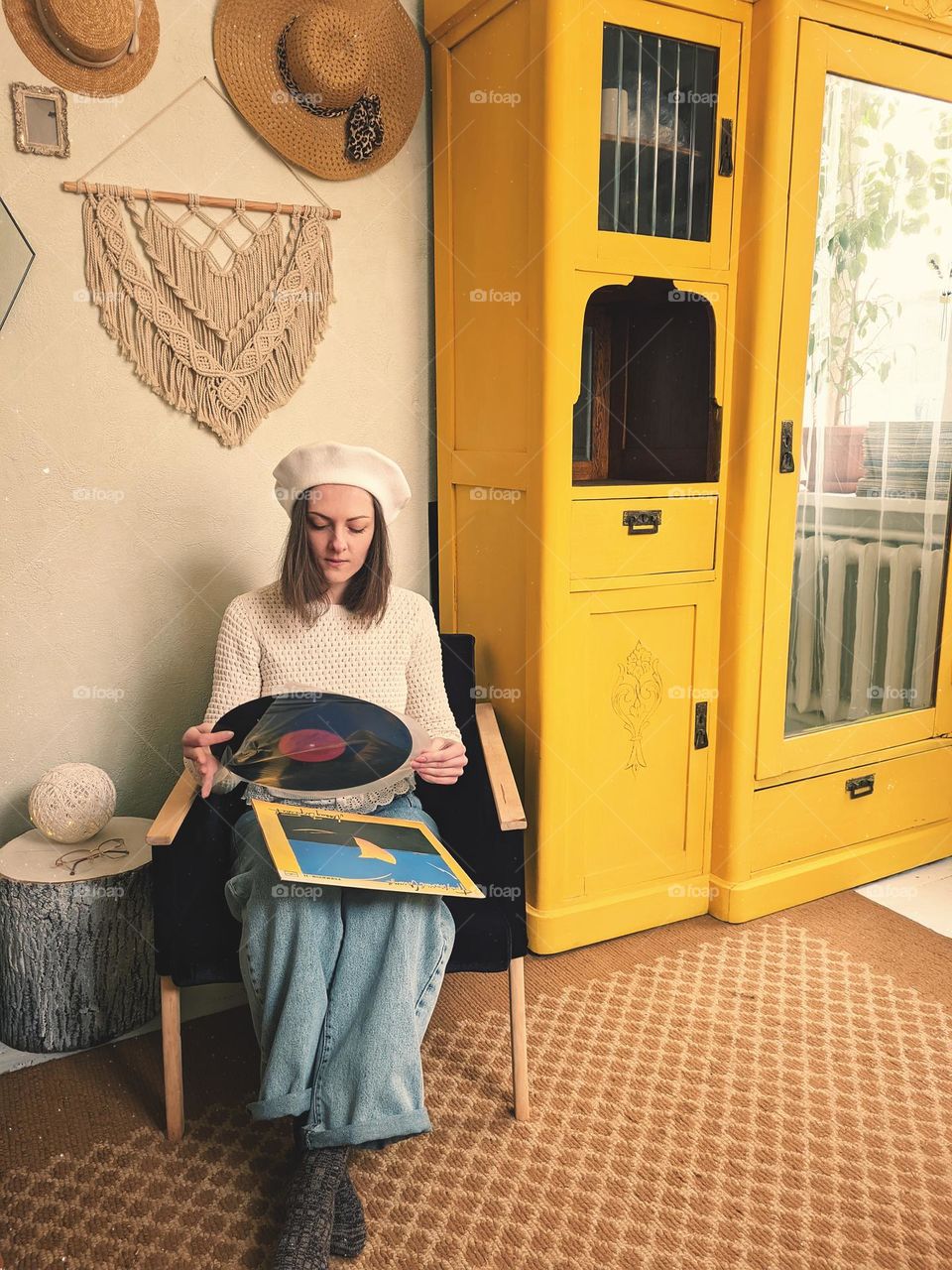 Portrait of beautiful young girl,  lady in beret sitting at cozy home in armchair near yellow vintage cabinet.  Vinyl music