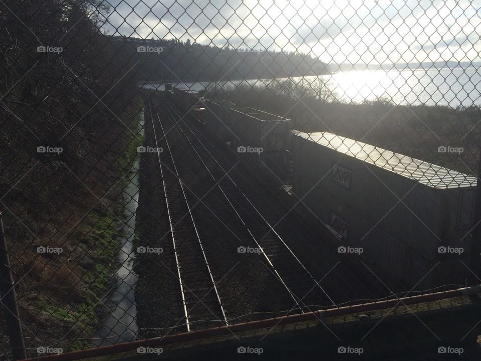 Train tracks along an ocean during sunset seen through a fence.
