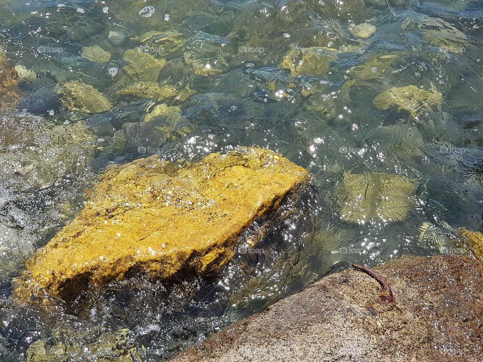 A beautiful scene of the sea water washing over a yellow lime rock as the tide goes out.