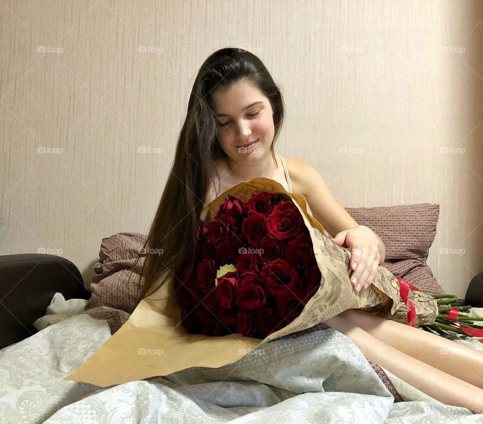 pretty girl sitting in bed with a huge bouquet of roses