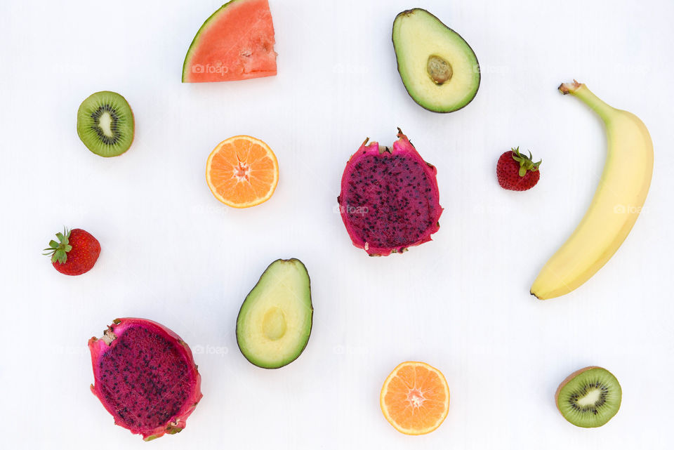 Bright flat lay of halved brightly colored fruits against a white background