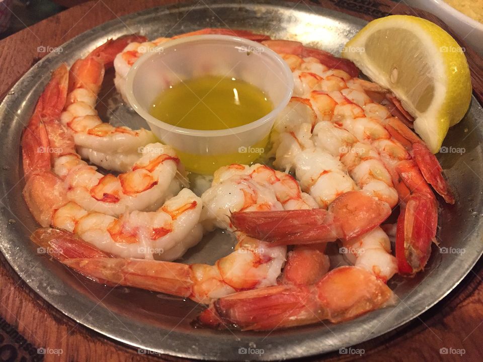 A platter of broiled shrimp with a lemon wedge and melted butter for dipping on the table at a seafood restaurant 