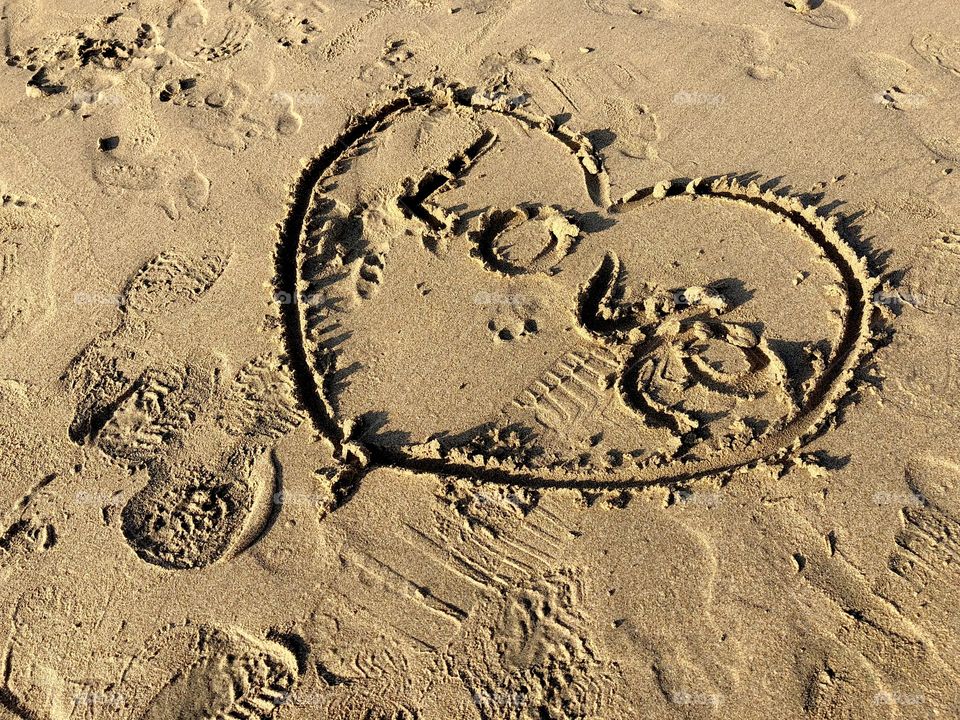 Love and heart finger drawing in the beach sand. Footprints. Brown overall color.