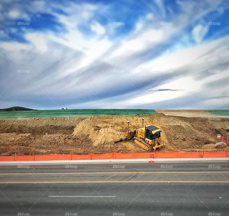A bulldozer pushes dirt uphill at a roadside grading project.