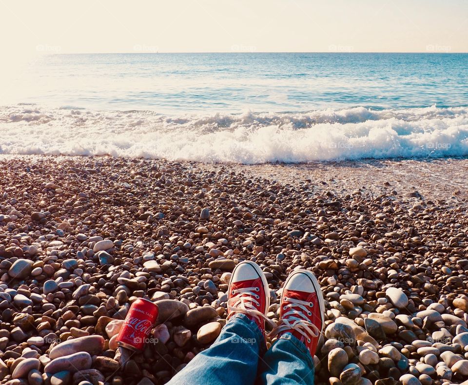 A can of Coca Cola on the beach with red sneakers.