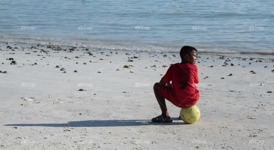 Kid take his rest after play football game on the beautiful summer beach