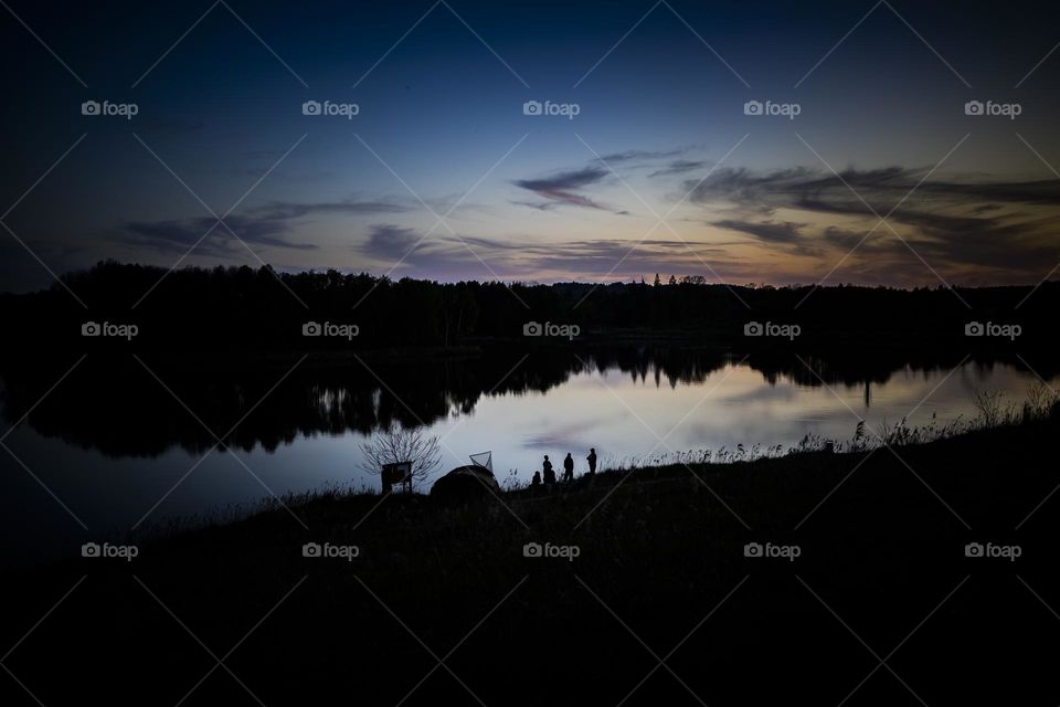Anglers on the lake in the evening during sunset. 