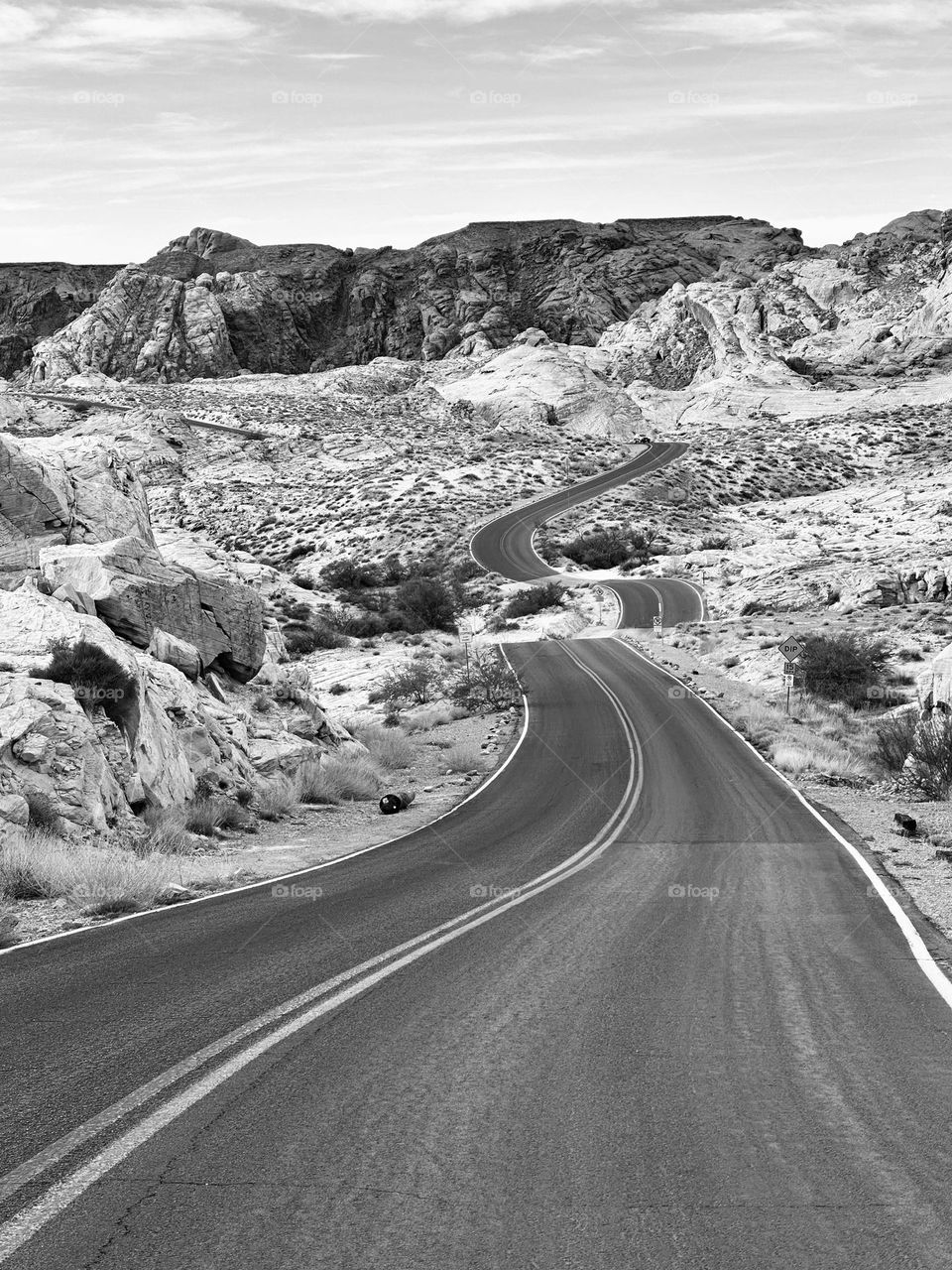 The black and white photo shows a 23.5 mile winding road through Valley of Fire State Park in Nevada. The road offers breathtaking views of the park's stunning red rock formations and desert landscapes. 
