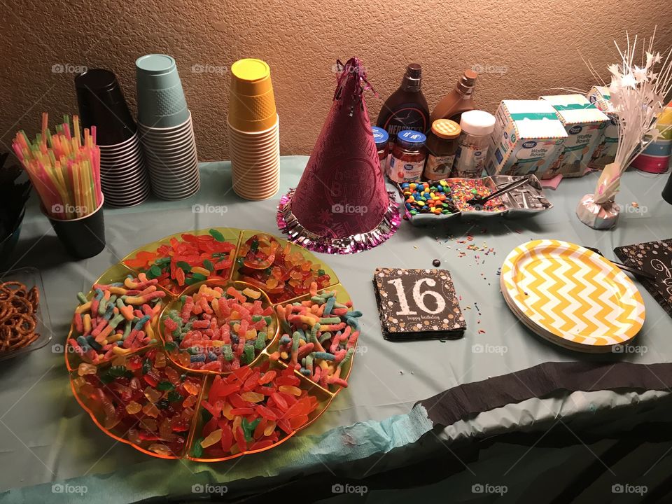 Celebrating a sweet 16 birthday. A beautiful display of colorful Birthday candies and party supplies and food displayed on a wooden table with a blue table cloth.