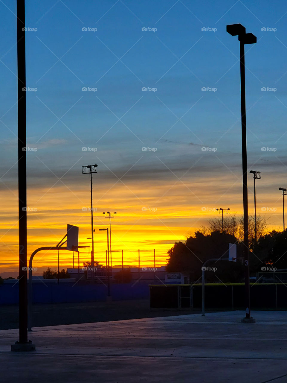 An athletic field lights and basketball hoop are highlighted against a beautiful Arizona sunset