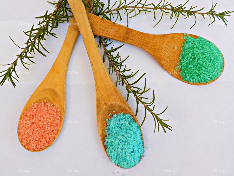 A flat lay is simply a photo of objects arranged on a flat surface, captured from directly above. This is a Flat lay of three different colors of salt on wooden spoons: pink, blue and green. greenery decor between spoons