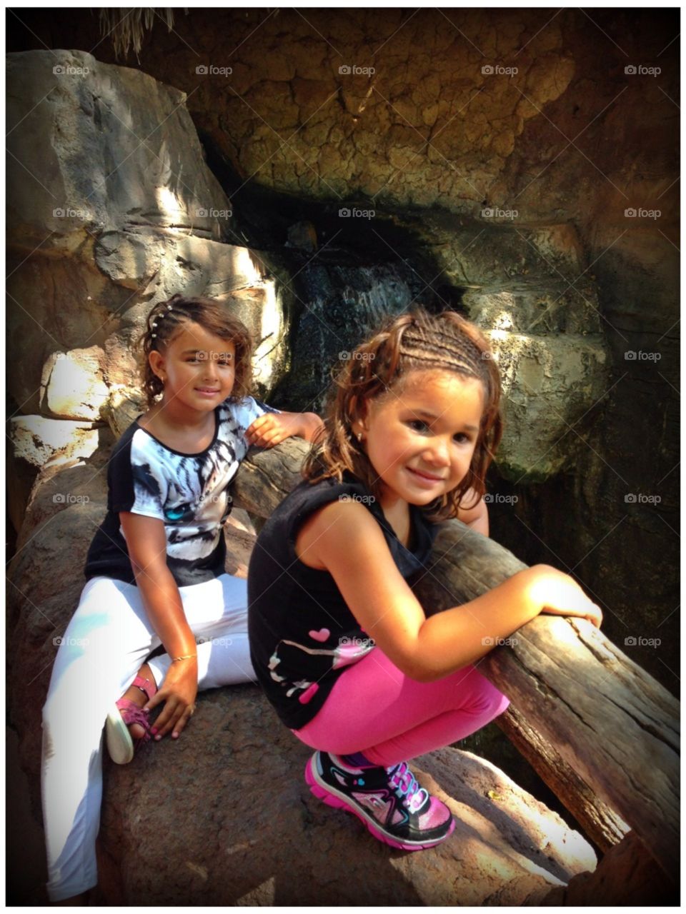 Close-up of two sisters sitting on rock