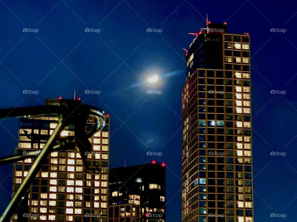 This is “Greenpoint”, Bklyn at “Newtown Creek” by the “Pulaski Bridge” in LIC, Queens with a misty glowing waxing moon in the sky that gives the surrounding illuminated high rise buildings competition with its light. 2023. Hypnotic Productions