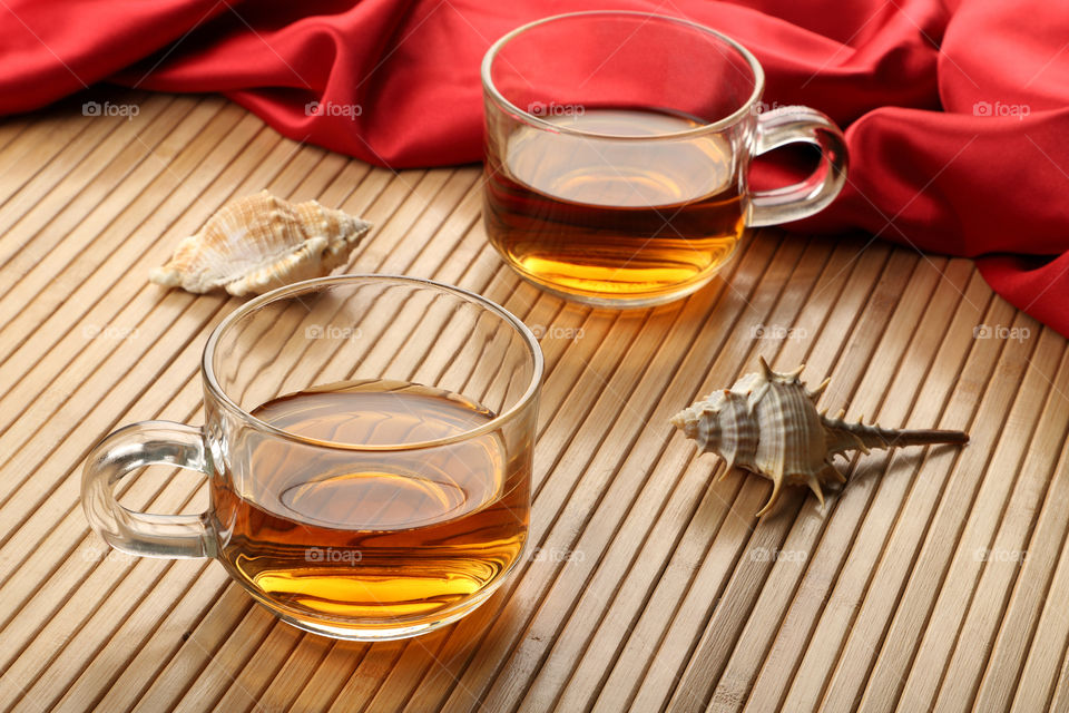 Two cups of hot tea on a wooden table with sea shells and satin cloth