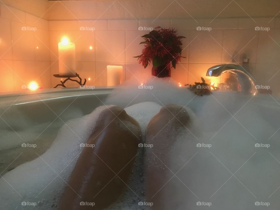 Woman relaxing in a luxurious bubblebath surrounded by golden candlelight.