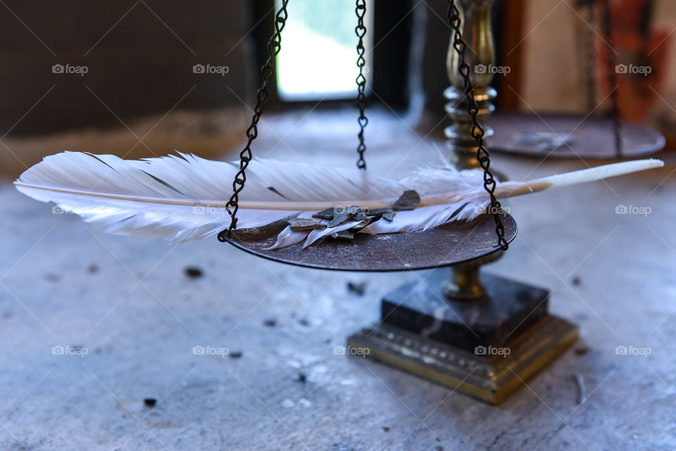 White feather and pebbles on a vintage scale with natural light coming in through a window in the background