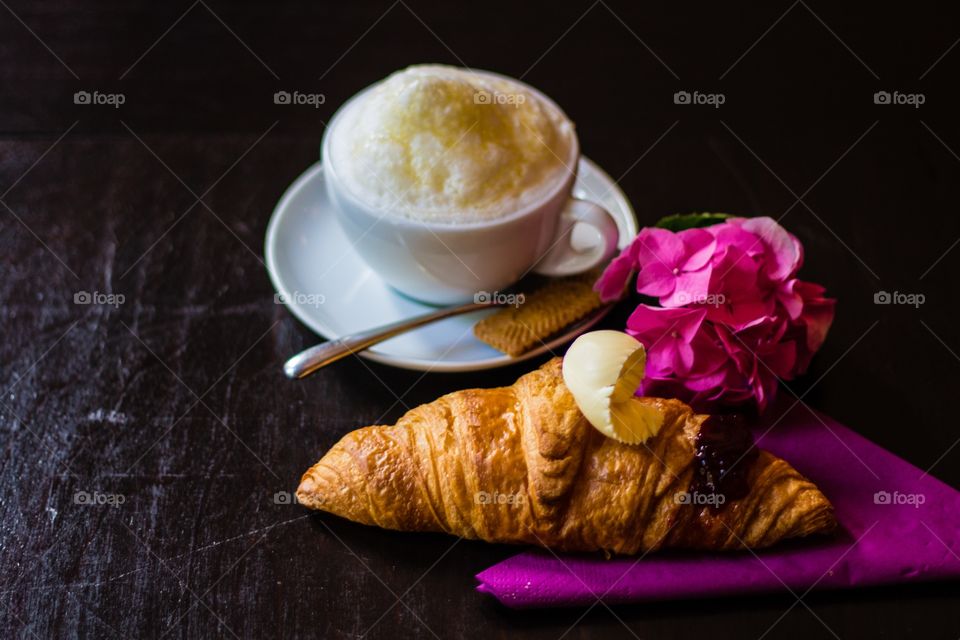 Topview of croissant with a flake of butter with a cup of cappuccino on wooden café table