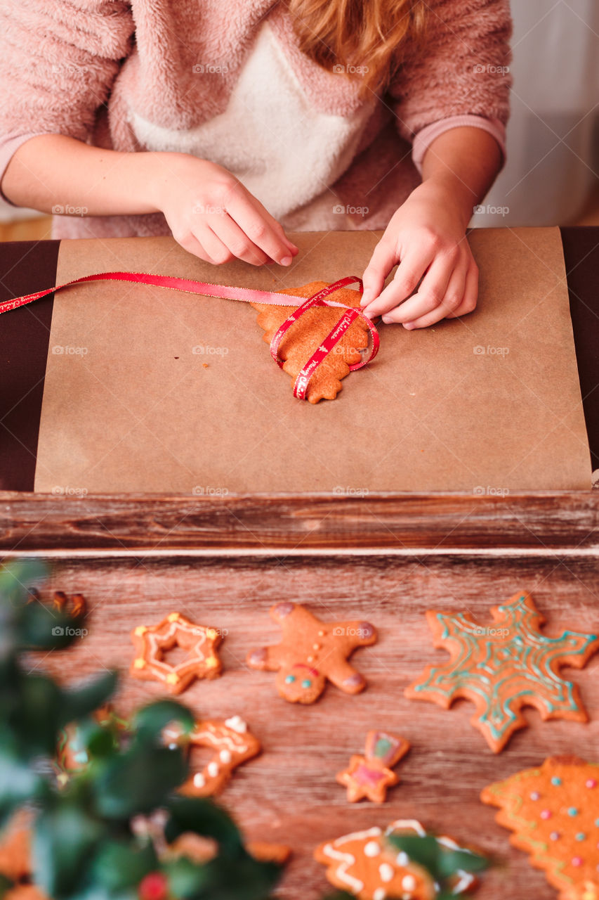 Girl tying baked Christmas gingerbread cookies with ribbon