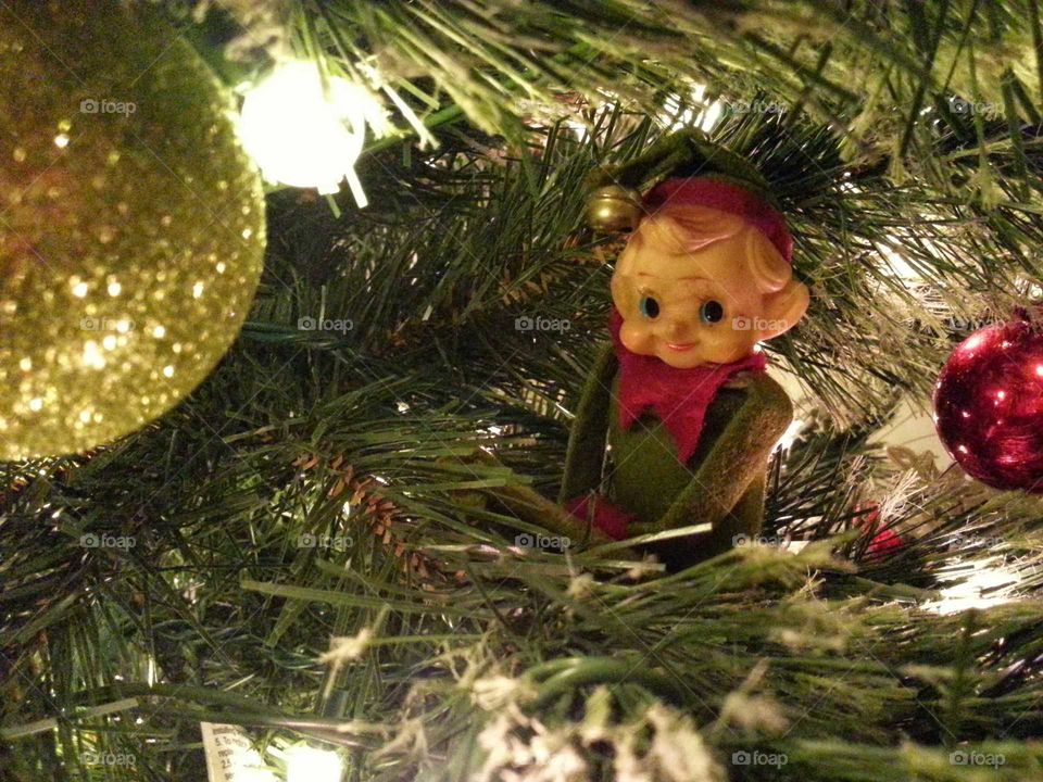 Antique Christmas elf hides in a pine tree awaiting the arrival of Santa among the ornaments.