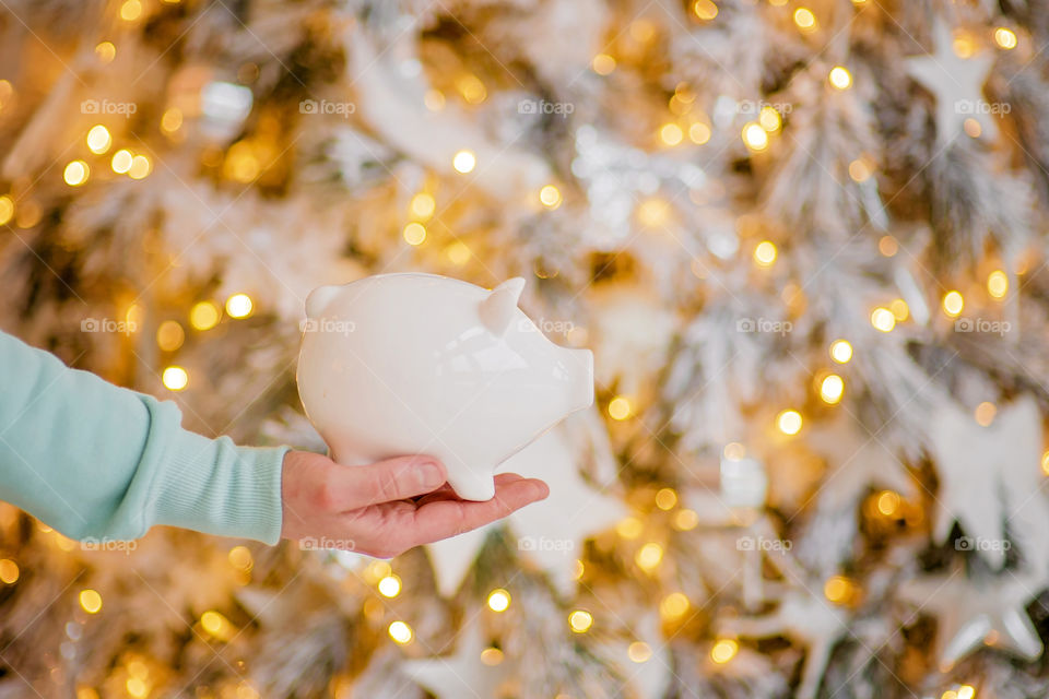 piggy bank with 100 dollars banknote in festive New Year atmosphere of scenery.  Magical bokeh with Christmas tree and bright lights.