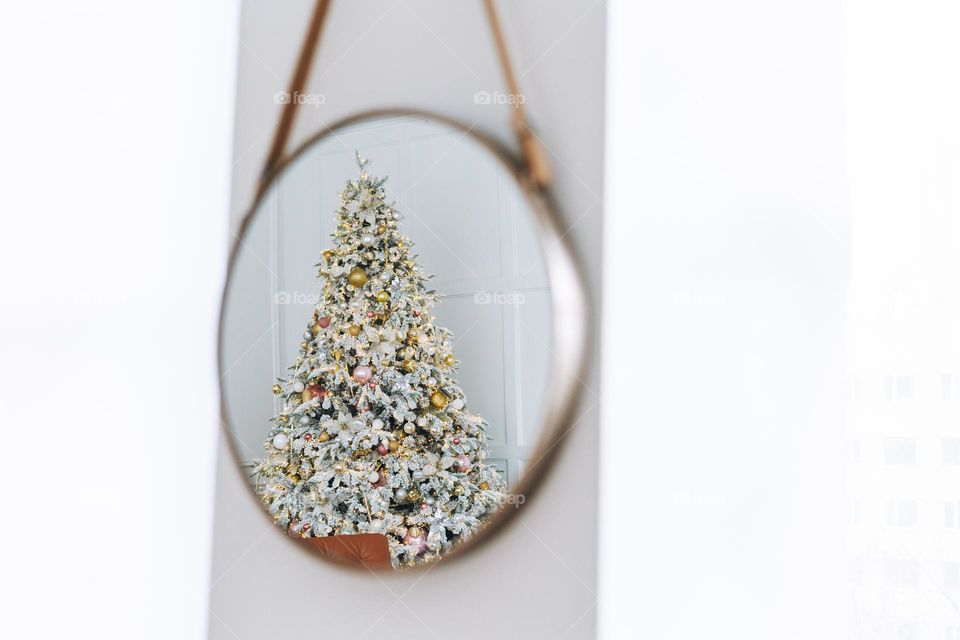 A decorated Christmas tree is reflected in the mirror at home