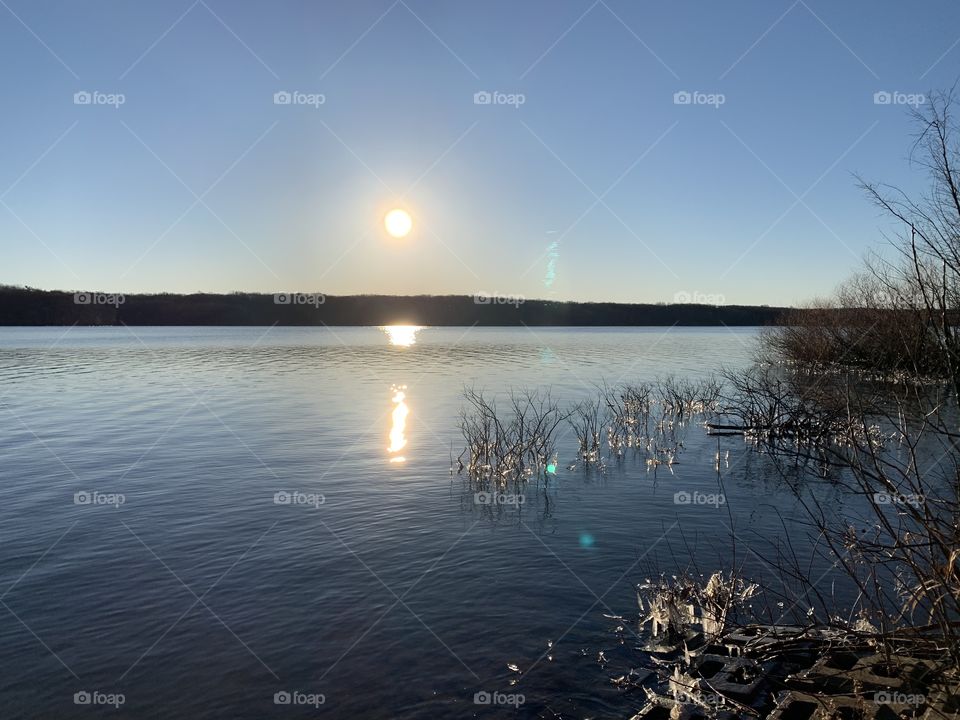 A view over the local reservoir on a very sunny morning. In the foreground, you can see ice on the weeds. 