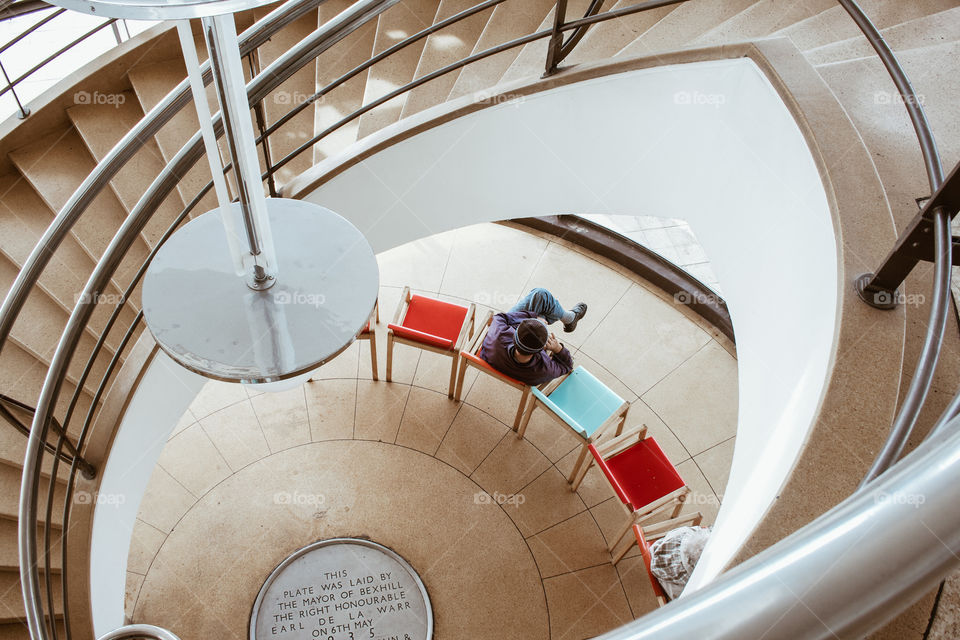 Downwards view inside a spiral staircase to people sitting on colourful seats on the lower floor 