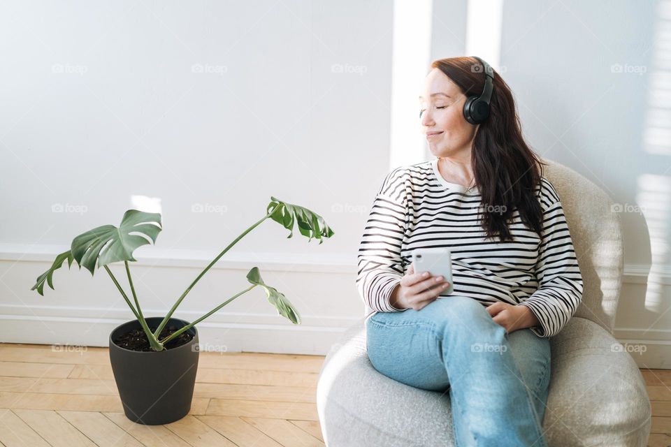 Young brunette woman with closed eyes in headphones listen music on mobile phone at home