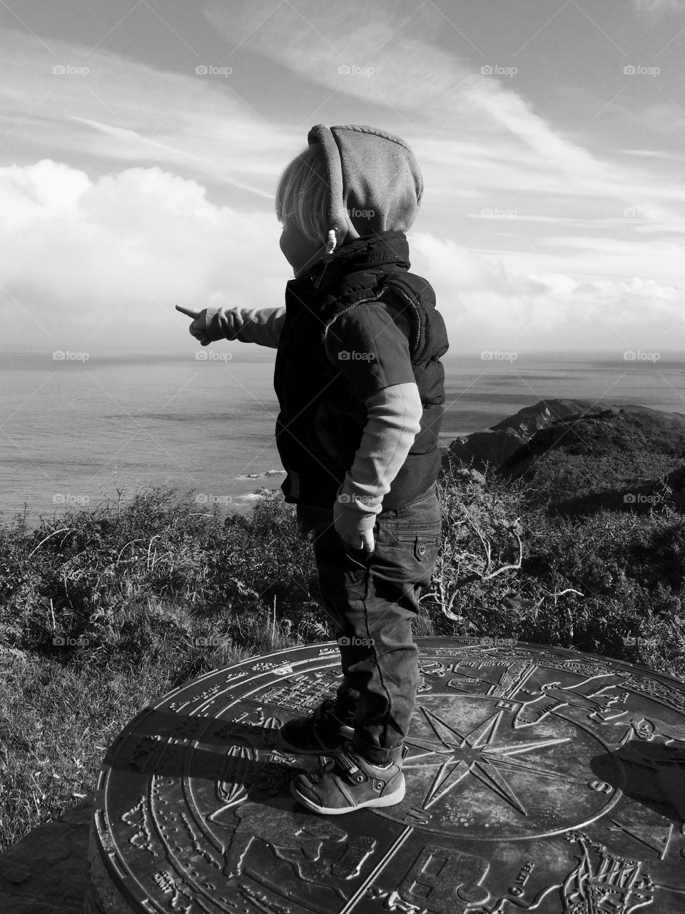 Boy standing on mountain pointing towards sea