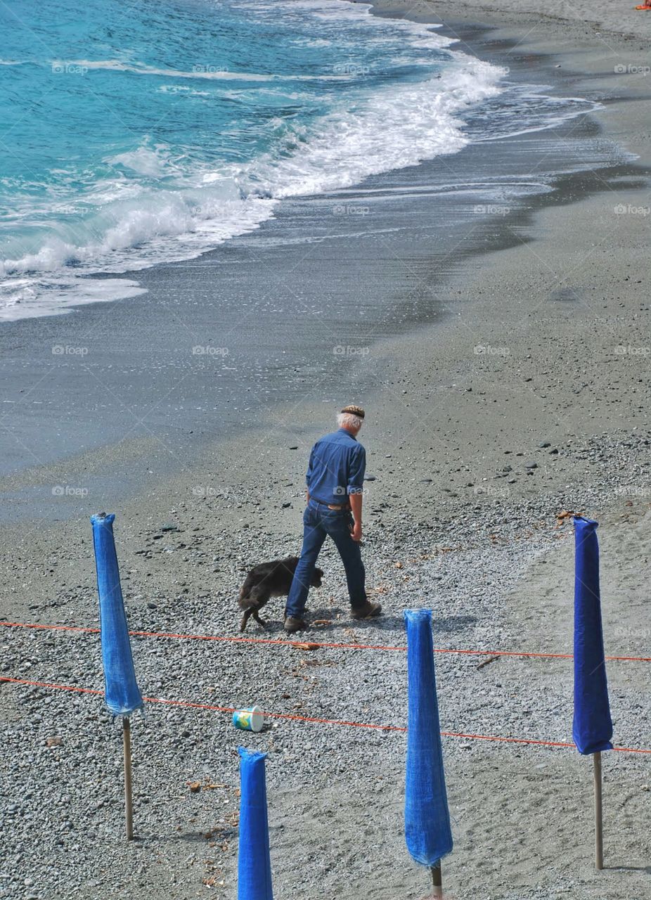 Beach comber and dog. A man walks along an empty beach with his black dog