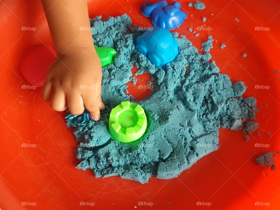 Hand of a kid playing with blue kinetic sand, close up