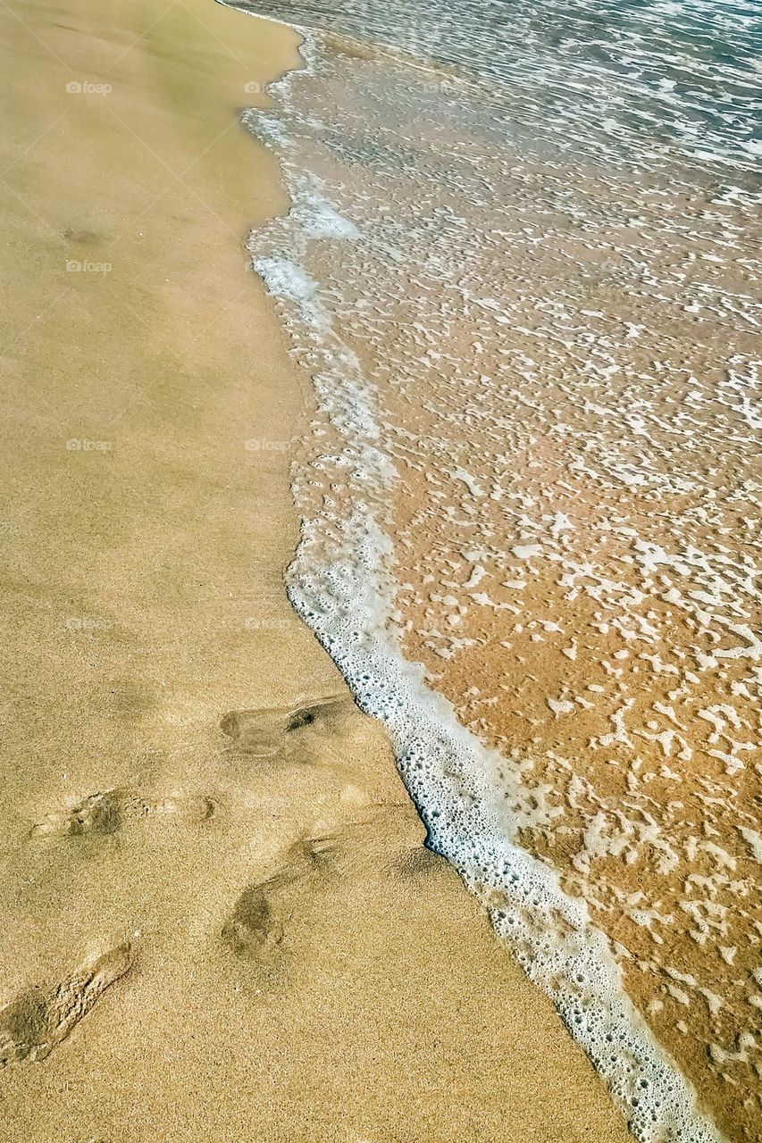 The coastline and footprints in the sand are in high angle view