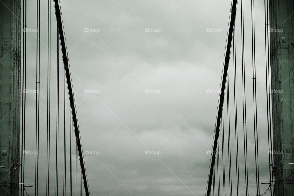Stormy clouds hover in the distance above the steel cable links of the George Washington bridge.