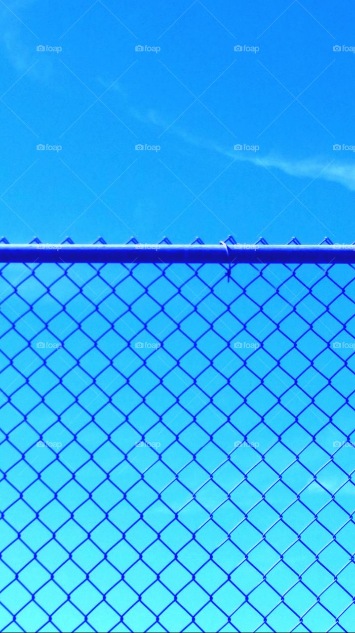 Blue sky shining behind a fence