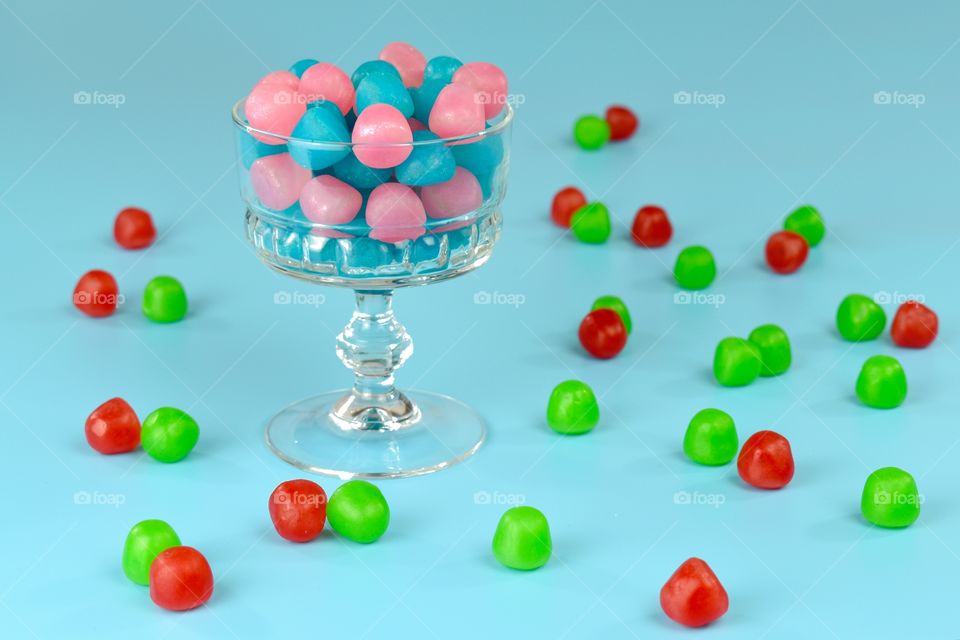 pink and blue candies in a glass cup with red and green candies around on a blue background