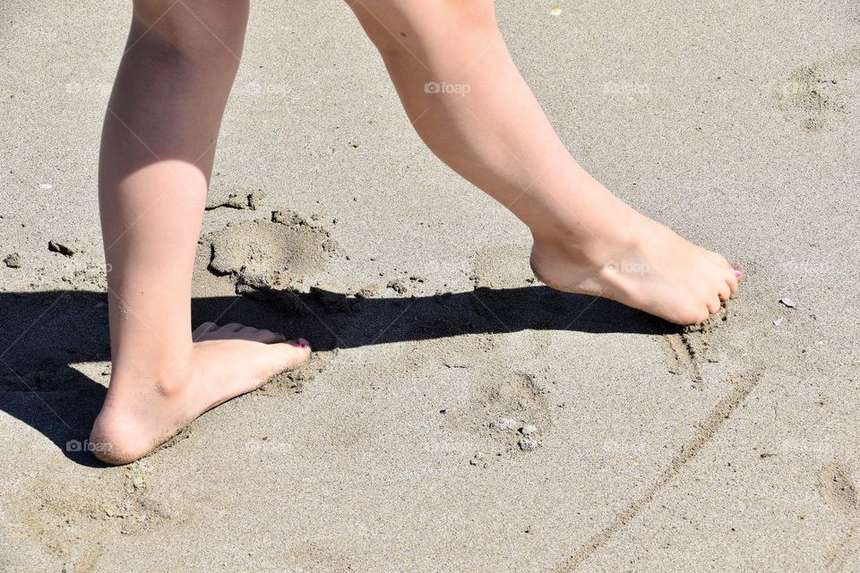 Feet drawing in sand . Beach game of a girl