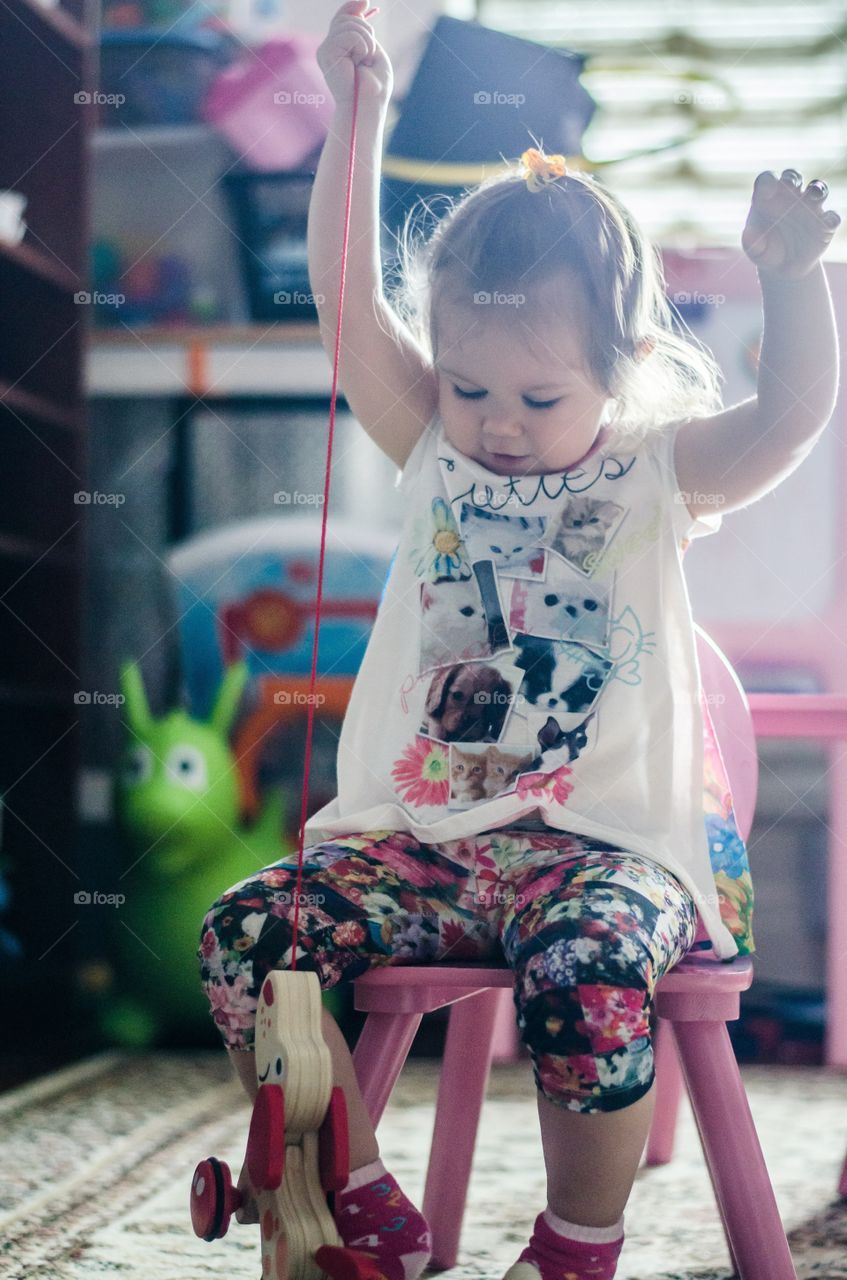 A little girl sitting on plastic chair with toy at home