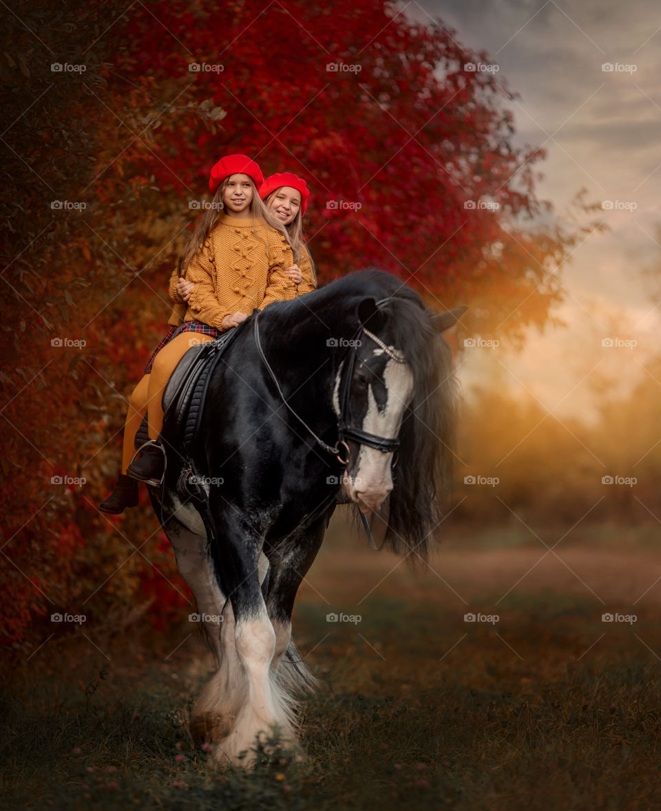 Twins girls on black stallion at autumn evening