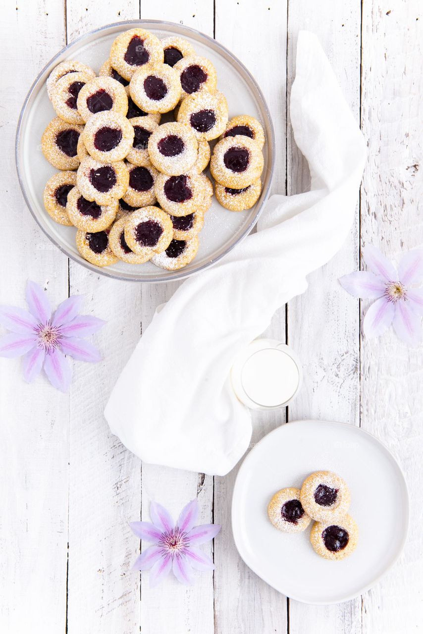 Flat lay of freshly baked raspberry thumbprint cookies with a glass of milk and summer flowers 