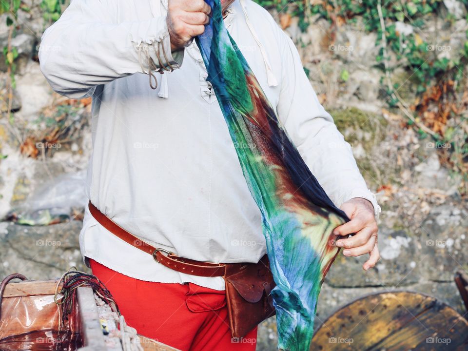 The man in the old national costume is showing process of dyeing fabric in italy