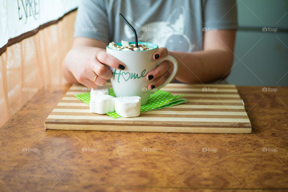 A girl in kaya drinks coffee with marshmallows in a cafe from a mug with the inscription at home