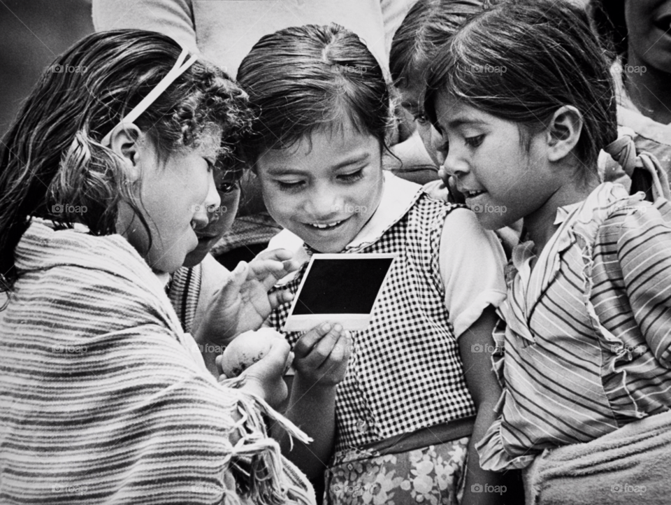 young school girls are intrigued by a polaroid photo as they watch it develop before their eyes. village in central mexico. central mexico by arizphotog