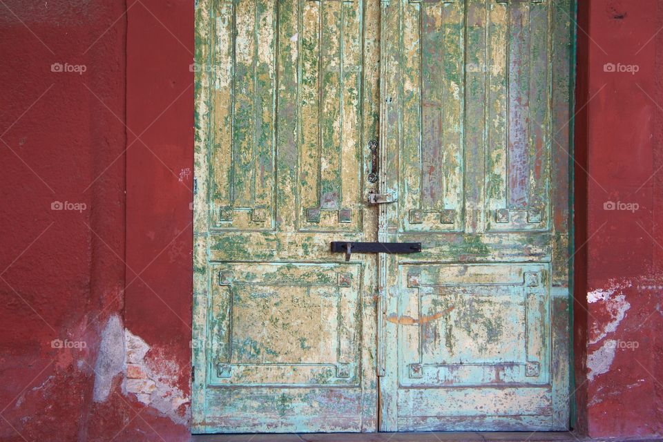 An interesting closed  doorway surrounded by colorful worn wall in San Miguel de Allende, Mexico.
